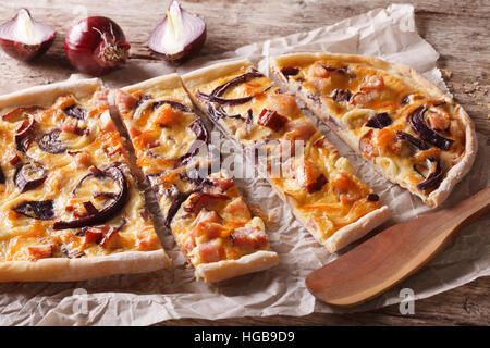 in Scheiben geschnitten Kuchen Flammkuchen mit Speck und roten Zwiebeln auf dem Papier. Horizontale closeup Stockfoto