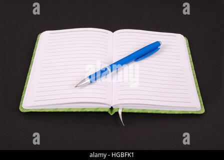 Weiße Notebook mit blauen Stift auf schwarzem Hintergrund isoliert Stockfoto