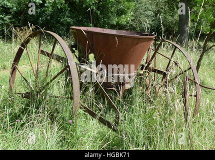 Rostige Oldtimer Landmaschinen lange Gras, Bäume im Hintergrund Stockfoto