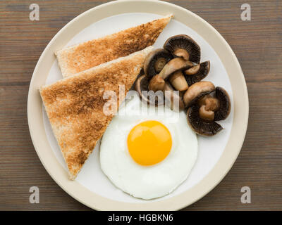 Gesundes Frühstück von einem einzigen Fried Egg Sunny Side Up Pilze und Toast serviert auf einem Teller mit einem Flach Zusammensetzung und keine Leute Stockfoto