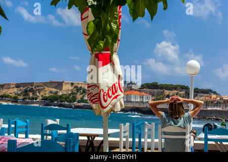 Eine Frau sitzt in einem Café mit Blick auf das Meer Rethymno, Kreta, Griechenland Stockfoto