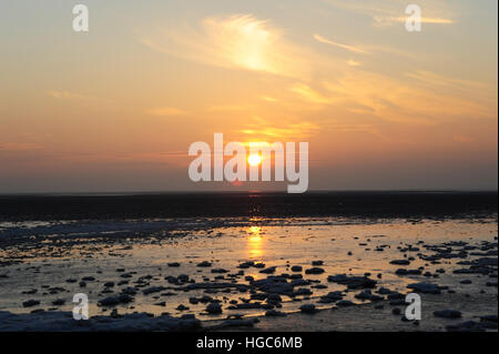 Blick über weite Strand mit Meer Eisblöcke, Roter Himmel gelb Sonne untergeht grauen Wolken Horizont, St Annes, Lancashire, UK Stockfoto