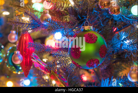 Christbaumschmuck.  Grün, Matte Oberfläche, Kugel mit Magenta Kreisen, glüht, umgeben von bunten Lichtern Mini. Stockfoto