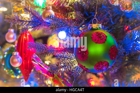 Christbaumschmuck.  Grün, Matte Oberfläche, Kugel mit Magenta Kreisen, glüht, umgeben von bunten Lichtern Mini. Stockfoto