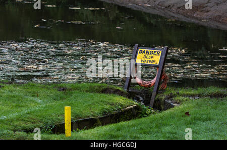 Ein Gefahrenzeichen und einen Rettungsring haben neben einem See Warnung über die Gefahren des Tiefenwassers aufgestellt. Stockfoto