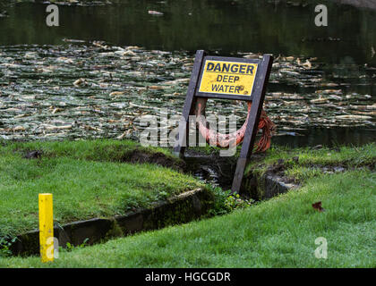 Ein Gefahrenzeichen und einen Rettungsring haben neben einem See Warnung über die Gefahren des Tiefenwassers aufgestellt. Stockfoto