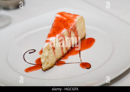 Stück Käsekuchen mit Erdbeer-Sauce und Chocolate Swirl Swirl auf weißen Teller Stockfoto