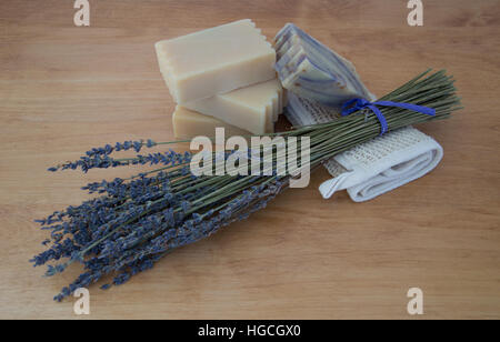 Nahaufnahme von vier Takte der Ziegen Milch Seife, eine von Lavendel auf Ramiefaser Waschlappen gemacht. Ein getrockneter Lavendel Bouquet ist auf Holztisch Stockfoto