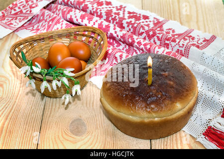 Auf dem Tisch liegen in einem Weidenkorb, bemalte Ostereier, Kuchen und künstliche Blumen. Stockfoto