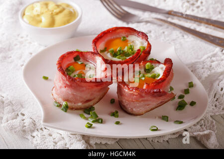 Spiegeleier, umhüllt von knusprigem Speck auf einem Teller und Sauce auf den Tisch. Horizontale Stockfoto