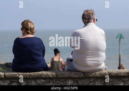 Dicker Mann und Frau sitzen auf Wand, Rückansicht Stockfoto