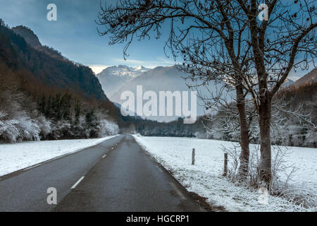 Einsame Straße, die durch tief verschneite Landschaft in Richtung Berge Stockfoto