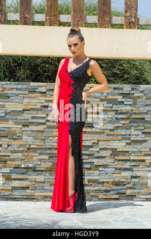 Schöne junge Frau in einem schwarzen und roten Kleid stehen im freien Hand an Hüfte Stockfoto