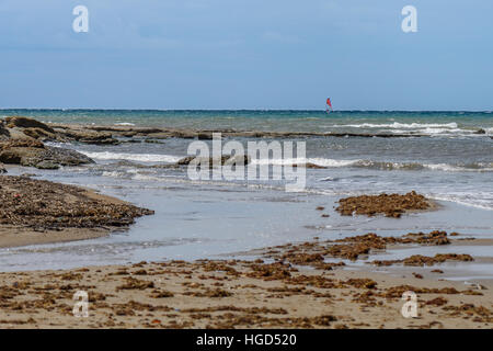 Seelandschaft im Mittelmeer mit Wolken und blauer Himmel, Teil des Strandes und weit entfernt ein windsurfer Stockfoto