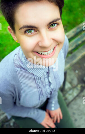 Hoch und breit Winkel Ansicht outdoor Portrait lustige kaukasischen Frau mit dunklen kurzen Haaren nach oben in die Kamera und lächelnd Stockfoto