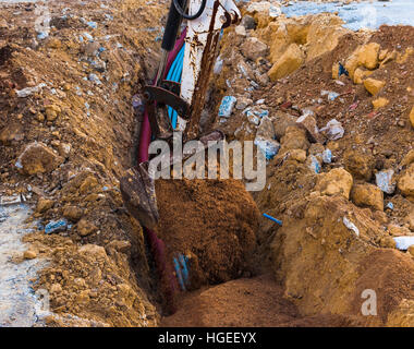 Bagger elektrische Leitungen mit Hilfe eines Arbeitnehmers mit Sand bedeckt. Stockfoto