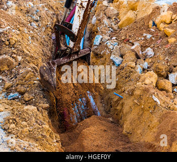 Bagger elektrische Leitungen mit Hilfe eines Arbeitnehmers mit Sand bedeckt. Stockfoto