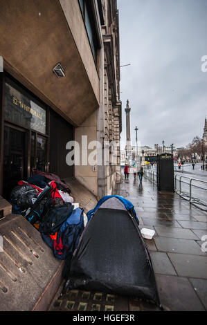 Ein Obdachloser, der in Whitehall campt, mit Trafalgar Square und Nelson's Column Beyond. Nass durch Regen Stockfoto