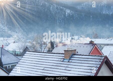 Frostiger Morgen in einem verschneiten Dorf. Rauchen Sie auf den Dächern der Häuser. Heizöl, Kohle und Holz. Stockfoto