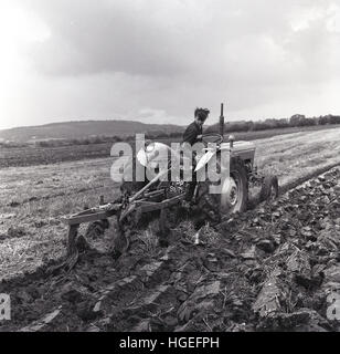 1960, historische, ein junger Mann auf einem Traktor Pflügen eines Feldes, ie drehen den Boden zu furchen. Stockfoto