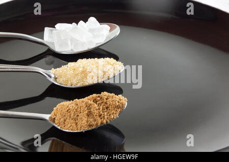 Brauner Rohrzucker und granulierter Zucker und Kandis in einem Metalllöffel auf dem schwarzen Hintergrund. Reiner Rohrzucker für natürliche. Stockfoto