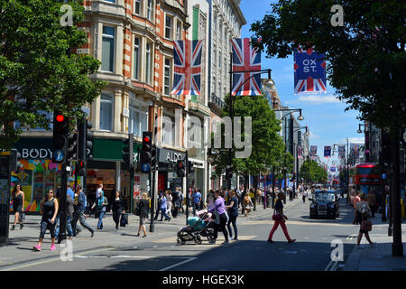 Oxford Street, London im Sommer mit Union Jack Flags, einem roten Bus, einem schwarzen Taxi und Menschen, die die Straße überqueren. Stockfoto