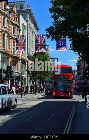 Oxford Street, London im Sommer. Die Straße ist mit Union Jack Flaggen dekoriert und ein roter Bus und ein hackney Taxi fahren die Straße hinunter. Stockfoto