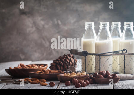 Vegane Milch aus Nüssen in Glasflaschen mit verschiedenen Nüssen auf alten hölzernen Hintergrund Stockfoto