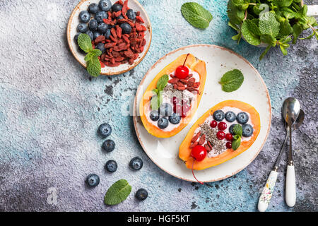 Saubere Lebensmittel für die Ernährung. Papaya mit Joghurt und Multi-Frucht, Chiasamen, Heidelbeere und Goji Beeren auf Platte über konkrete Hintergrund. Ansicht von oben Stockfoto