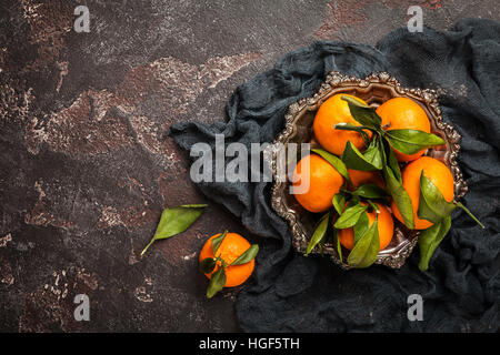 Frische Mandarinen mit Blättern in Metallschale auf dunklem Hintergrund. Draufsicht mit Textfreiraum. Stockfoto