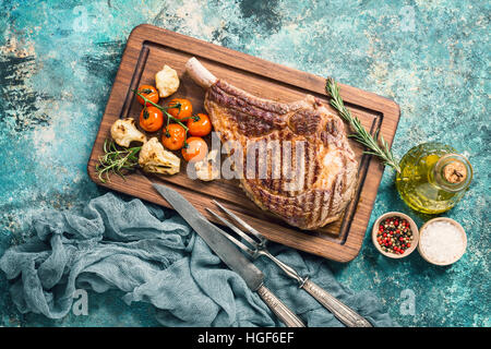 Saftig gegrillte Tomahawk Rindersteak mit Knochen mit Gewürzen, frischem Rosmarin und Grillgemüse auf Schneidebrett, Ansicht von oben Stockfoto