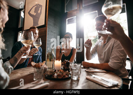 Heterogene Gruppe von jungen Menschen, die Wein im Restaurant. Männer und Frauen treffen in einem Restaurant zum Abendessen. Stockfoto