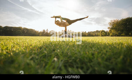 Mann und Frau paar Yoga im Freien auf dem Rasen zu tun. Passen Sie junges Paar üben Acroyoga. Mann heben und balancing Frau auf einem Bein im Park. Stockfoto