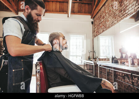 Barber Verkleidung Client mit Salon Kap vor dem Haarschnitt. Friseur bei der Arbeit mit Mann auf Stuhl sitzend. Stockfoto