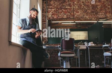 Friseur mit digital-Tablette in seinem Shop. Friseur am Friseur arbeitet an digital-Tablette sitzen. Stockfoto