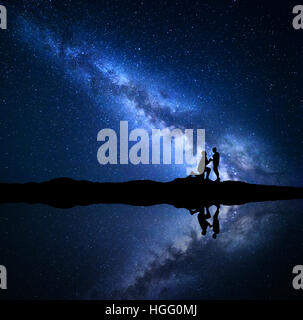 Milky Way. Silhouetten von einem Mann macht Heiratsantrag an seine Freundin auf dem Berg in der Nähe von See Stockfoto