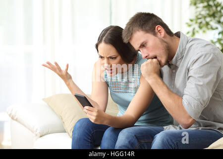 Wütend paar mit Handy sitzen auf einer Couch im Wohnzimmer zu Hause Stockfoto