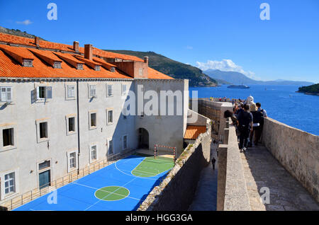 Touristen Fuß entlang der Wand der ummauerten Stadt von Dubrovnik, Kroatien, vorbei ein Korbball Gericht Zugehörigkeit zu einer lokalen Schule. Stockfoto