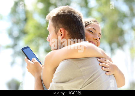 Betrüger SMS mit seinem anderen Liebhaber am Telefon und umarmt seine unschuldige Freundin Stockfoto