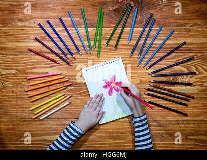 Des Kindes Hände Rawing eine Blume auf einem Notebook mit Farbstiften herum auf dem Holztisch Stockfoto