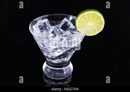 Prickelnde Getränke in einem Martini-Glas mit einer Limettenscheibe auf schwarzem Hintergrund Stockfoto
