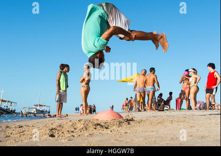 BAHIA, Brasilien - 6. Februar 2016: Junger brasilianische Mann führt akrobatische Flip am Ufer von einem abgelegenen Strand. Stockfoto