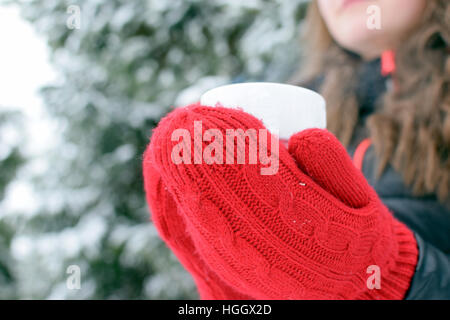 Frau mit roten Fäustlingen, die im Winter eine Tasse mit heißem Tee, Kaffee oder Schokolade hält. Stockfoto