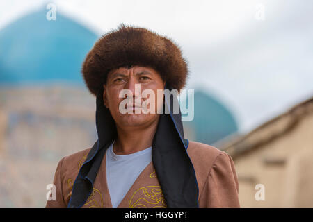 Kasachische Mann in Trachten mit den blauen Kuppeln des Khoja Ahmed Yasawi Mausoleums im Hintergrund, Turkestan, Kasachstan Stockfoto