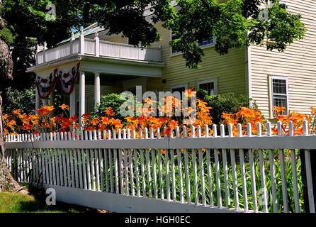 Fitzwilliam, New Hampshire - 11. Juli 2013: Bright orange Day Lillies flankieren einen weißen Lattenzaun vor der Fitzwilliam Public Library Stockfoto