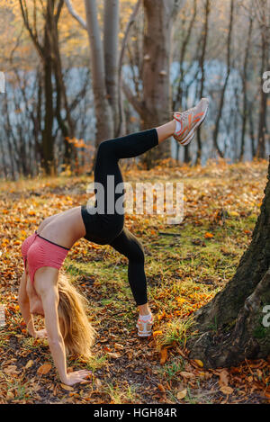 schöne erstaunliche Frau tun stretching Übungen im Freien im Park. Weibliche Sportmodell Ausübung Herbst Outdoorpark. flexible Mädchen hat eine Ausbildung in Holz Stockfoto