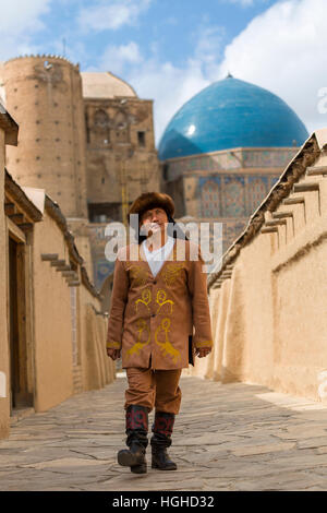 Kasachische Mann in Trachten mit den blauen Kuppeln des Khoja Ahmed Yasawi Mausoleums im Hintergrund, Turkestan, Kasachstan Stockfoto