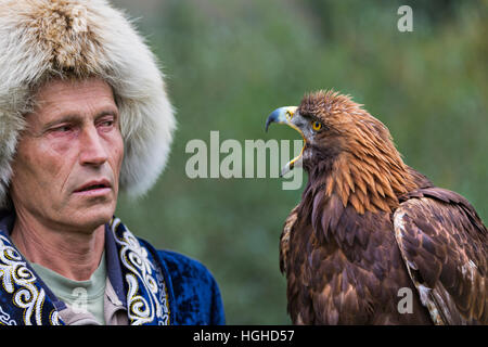 Kasachische Adler Jäger in traditionellen Kostümen hält seine Goldeneagle und sie schauen einander in Almaty, Kasachstan. Stockfoto