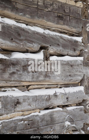 Eine festliche Winter Hintergrund mit verwitterten silbrig graue horizontale gesägte Stämme mit Schnee dazwischen.   Protokolle-Winkel in Richtung der Ecke des Gebäudes. Stockfoto