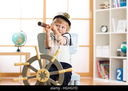 Kind junge gekleidet Kapitän oder Seemann spielt auf Stuhl als Schiff in seinem Zimmer. Kind schaut durch Teleskop. Stockfoto